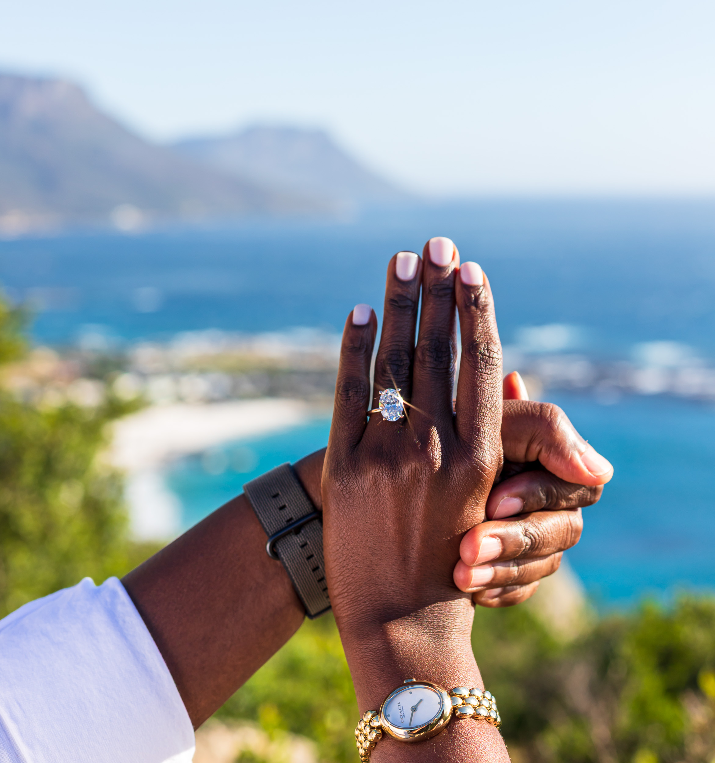 Hands held together, showing the engagement ring against the coastline