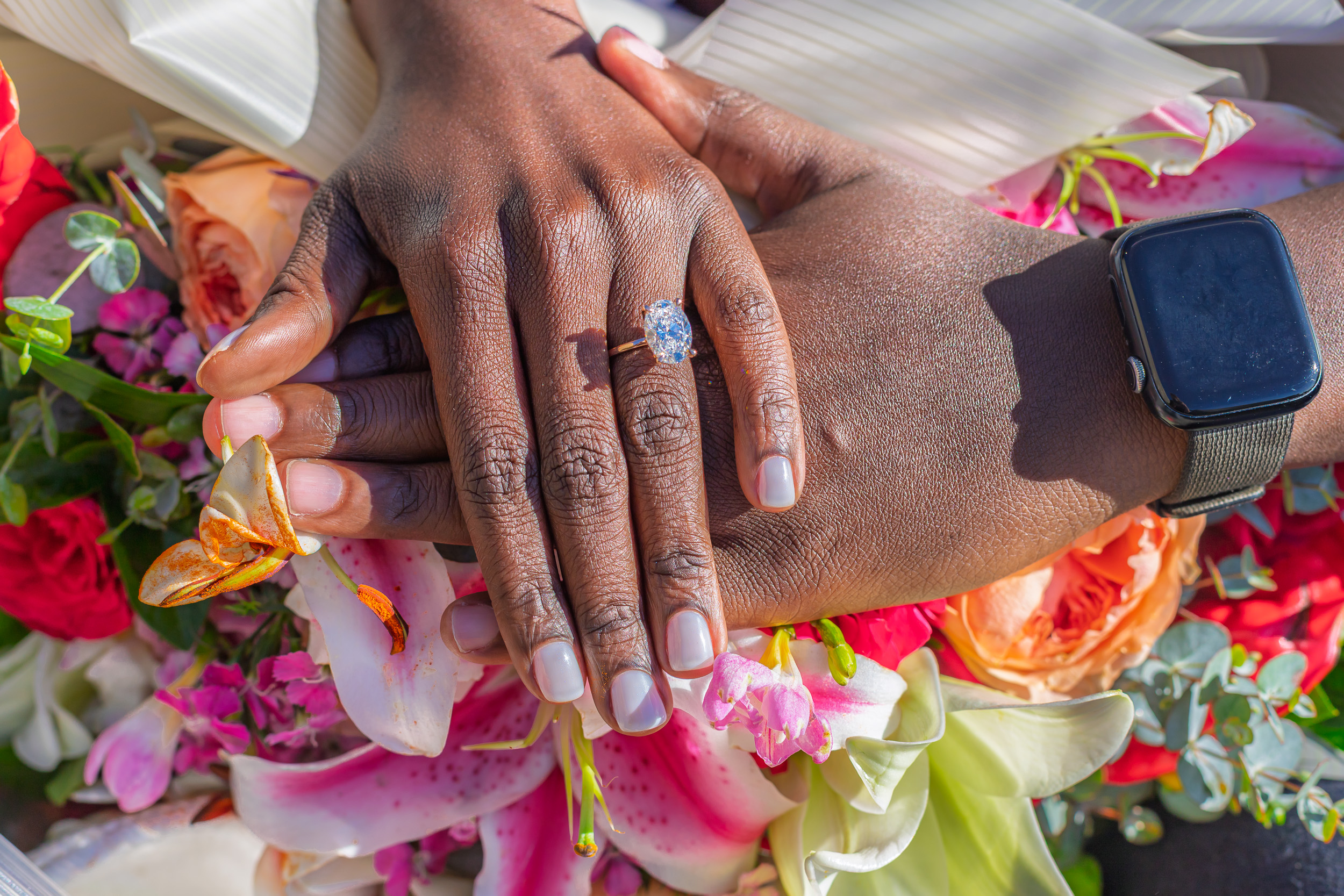 The engagement ring and joined hands over a colourful bouquet
