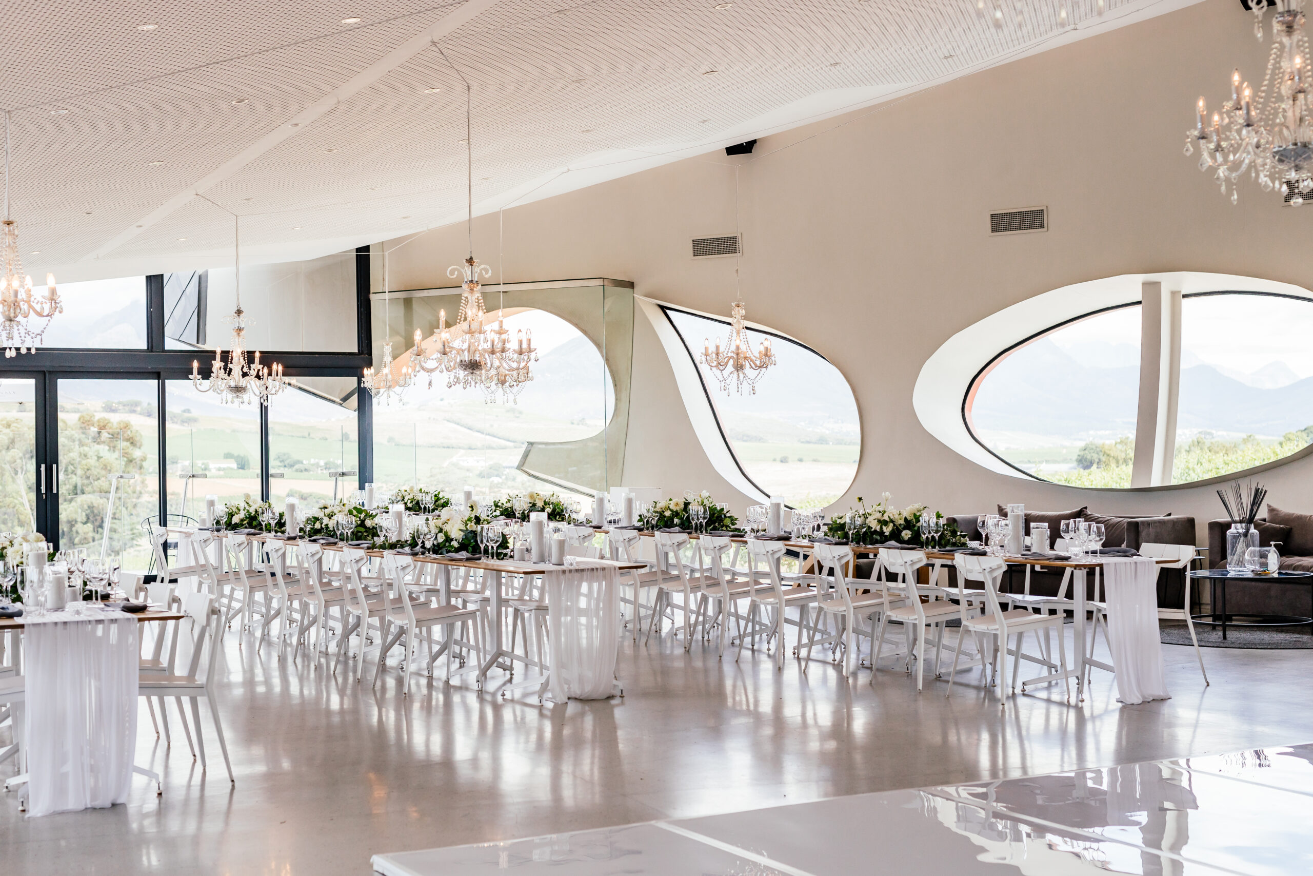 Louisvale’s reception space with chandeliers, white tables and curved windows overlooking the vineyards